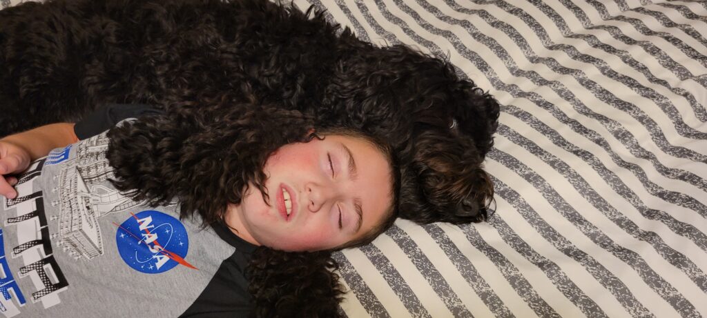 Kiddo and doggy sleeping on striped comforter on bed.