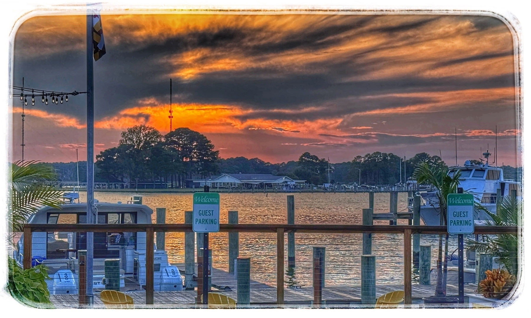 A vibrant sunset casts colorful reflections over a tranquil marina with boats docked and guest parking signs visible.