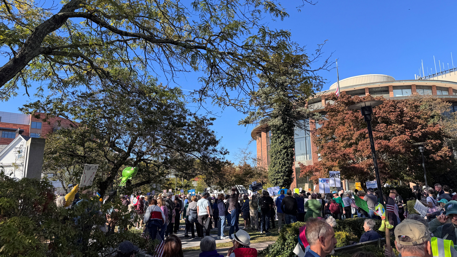 A group of people is gathered outdoors at the old Court House in Doylestown in a park-like setting, with trees and a large building in the background.