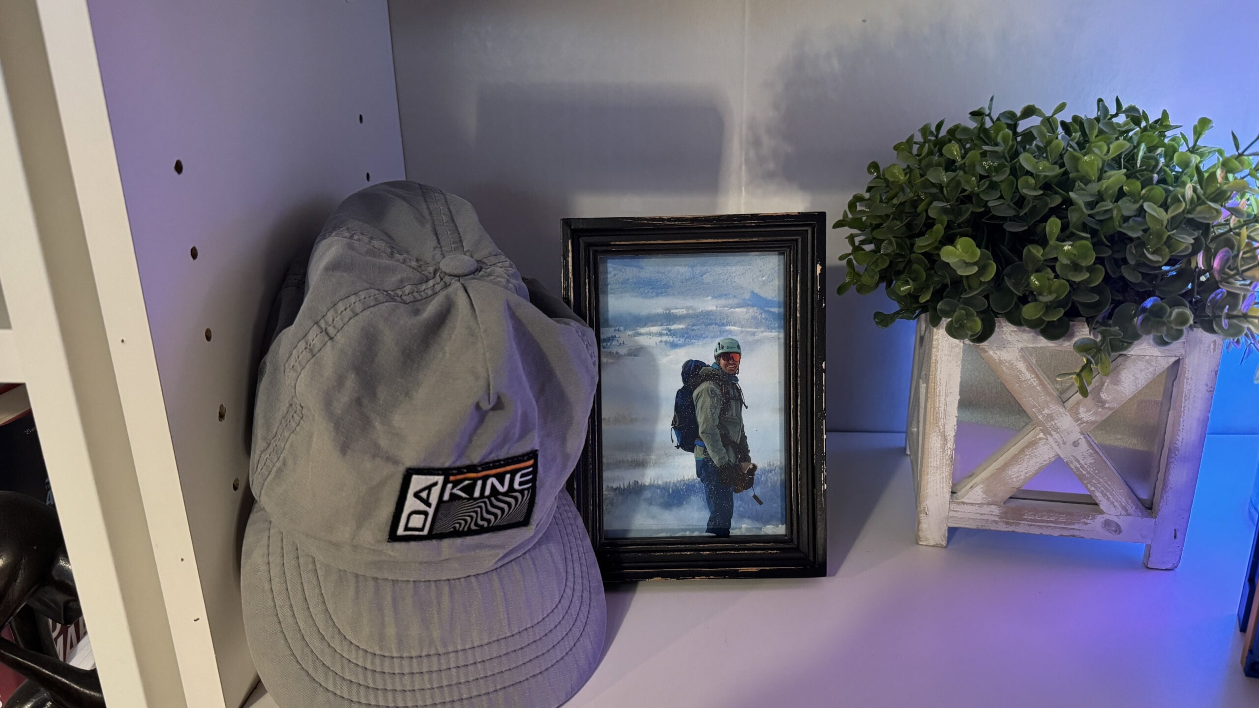A little shelf area with my late brother's hiking hat and a picture of him in the mountains and a fake decorative plant from Home Goods.