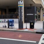 Entrance sign for Farragut West Station on a city street, with a mailbox nearby.