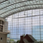 Large indoor atrium with a curved glass roof and a view of an urban landscape beyond.