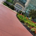 A hand holding a Starbucks cup in front of a modern glass building with landscaped gardens.