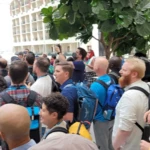 A diverse group of people in a hotel atrium, gathered and looking in one direction.